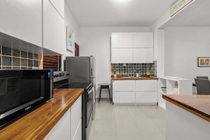 A compact kitchen with a microwave, oven, and refrigerator. - Vida Luna | Cozy Old San Juan Retreat + Terrace (San Juan)