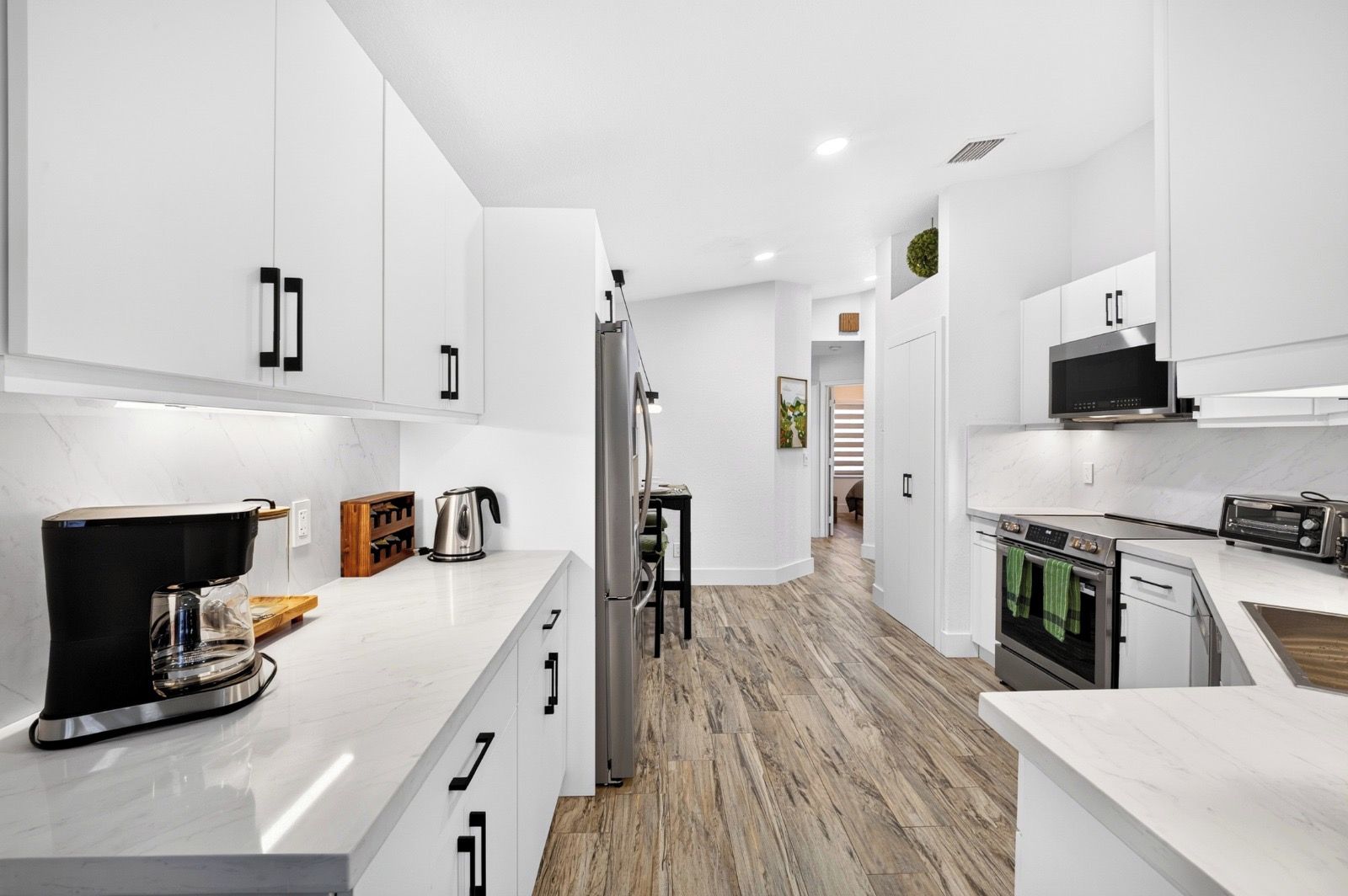 A modern kitchen with white cabinetry, a coffee machine, a kettle, a microwave, an oven, and a toaster.