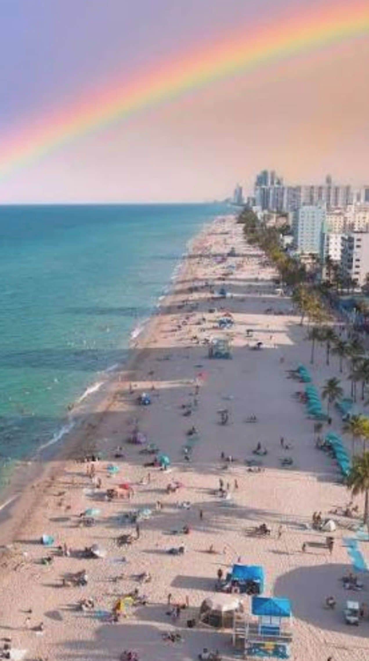 Una playa con un arcoíris, personas y edificios al fondo.