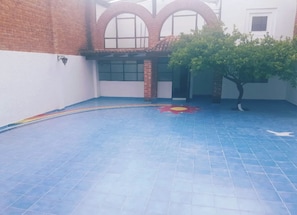 A courtyard with a tiled floor, a tree, and a building with arched windows.
