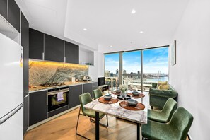 A modern kitchen with a marble countertop and a dining area with a city view. - Harbour View 1BR Escape | Pool, Gym & Sauna (Melbourne)