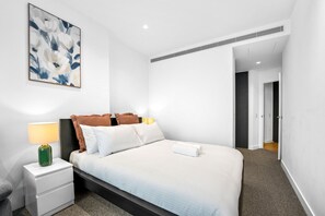 A modern hotel room with a bed, bedside tables, a lamp, and a painting on the wall. - Harbour View 1BR Escape | Pool, Gym & Sauna (Melbourne)
