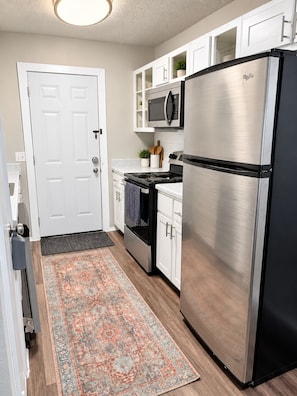 A kitchen with a stainless steel refrigerator, a microwave, and a stove. There is a patterned rug on the floor and a white door. - SOCO 2BDR-Shoping, Dining, Music - Apartment (Austin)
