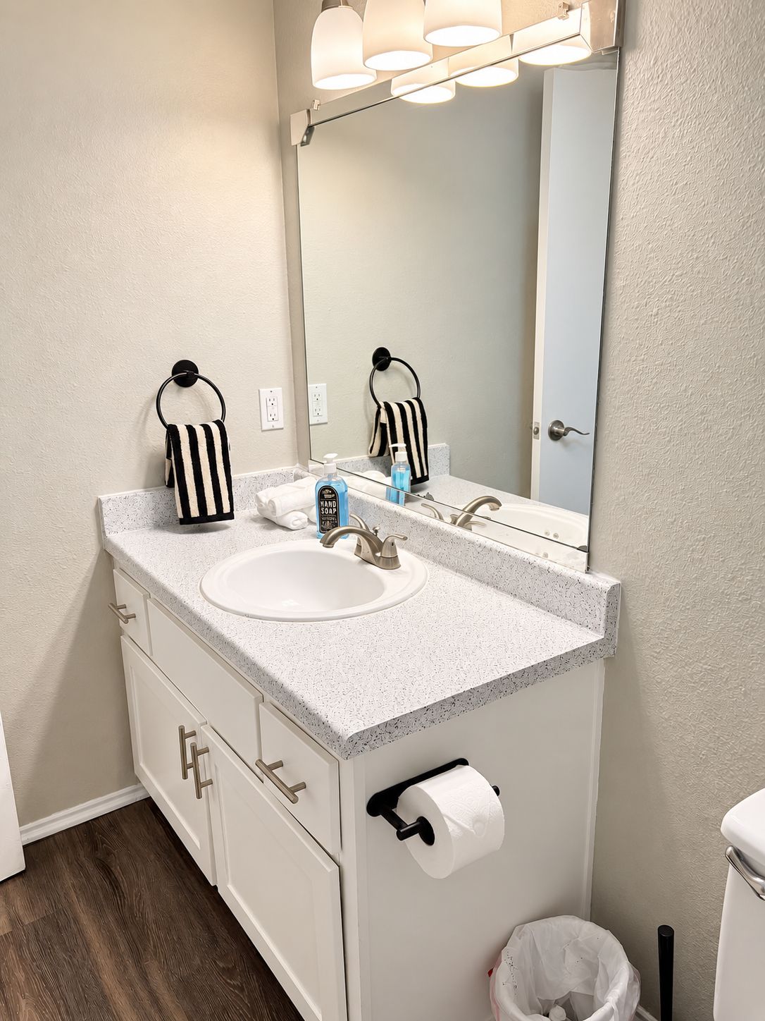 A bathroom with a white sink, a mirror, a towel rack, a toilet paper holder, and a trash can.
