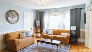 A living room with two sofas, a coffee table, a rug, a chandelier, and a door. - Large Apartment Between Bates, St. Mary’s & CMMC (Lewiston)