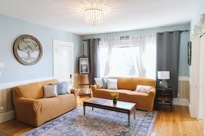 Ein Wohnzimmer mit zwei Sofas, einem Couchtisch, einem Teppich, einer Chandelier und einer Tür.