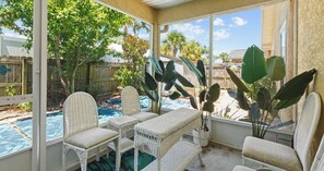 A covered patio with wicker furniture, a pool, and tropical plants. - Pinetree Palace - 4BR Cozy Home (Panama City Beach)