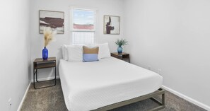A bedroom with a bed, two nightstands, a window, and two wall-mounted artworks. - Pinetree Palace - 4BR Cozy Home (Panama City Beach)