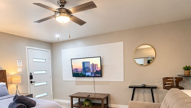 Ein modernes Schlafzimmer mit Bett, Sofa, Deckenventilator, Fernseher, Spiegel und einem kleinen Tisch.