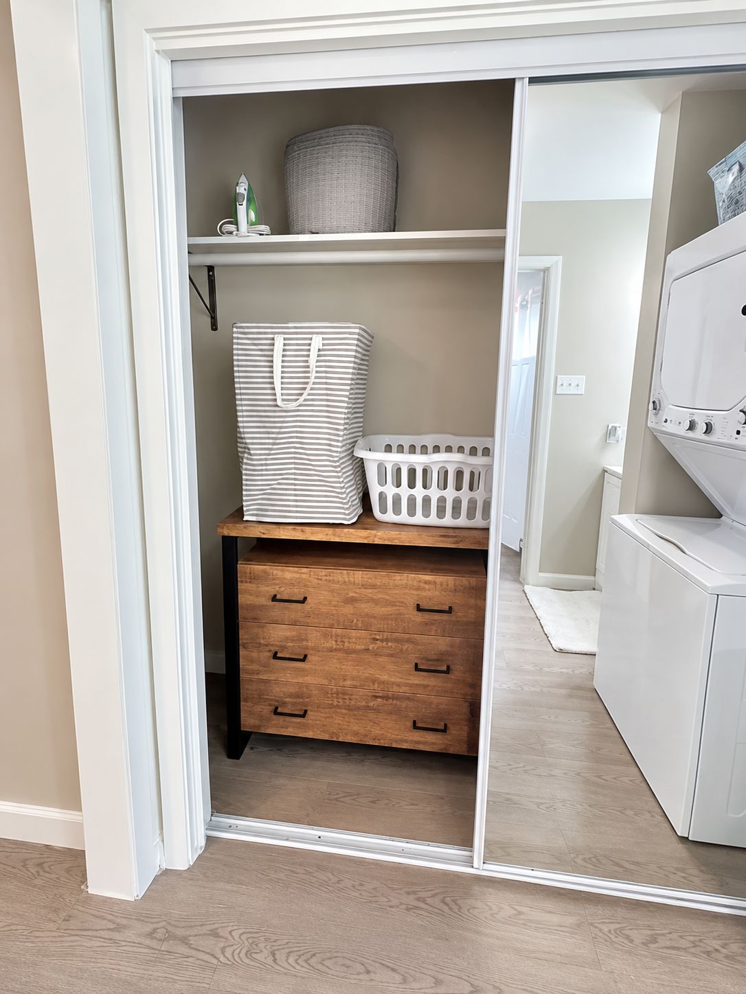 A closet with a mirrored door, a wooden dresser, and a laundry basket.