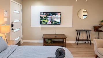 A hotel room with a bed, a television mounted on the wall, a ceiling fan, a small table with a plant, and a round mirror.