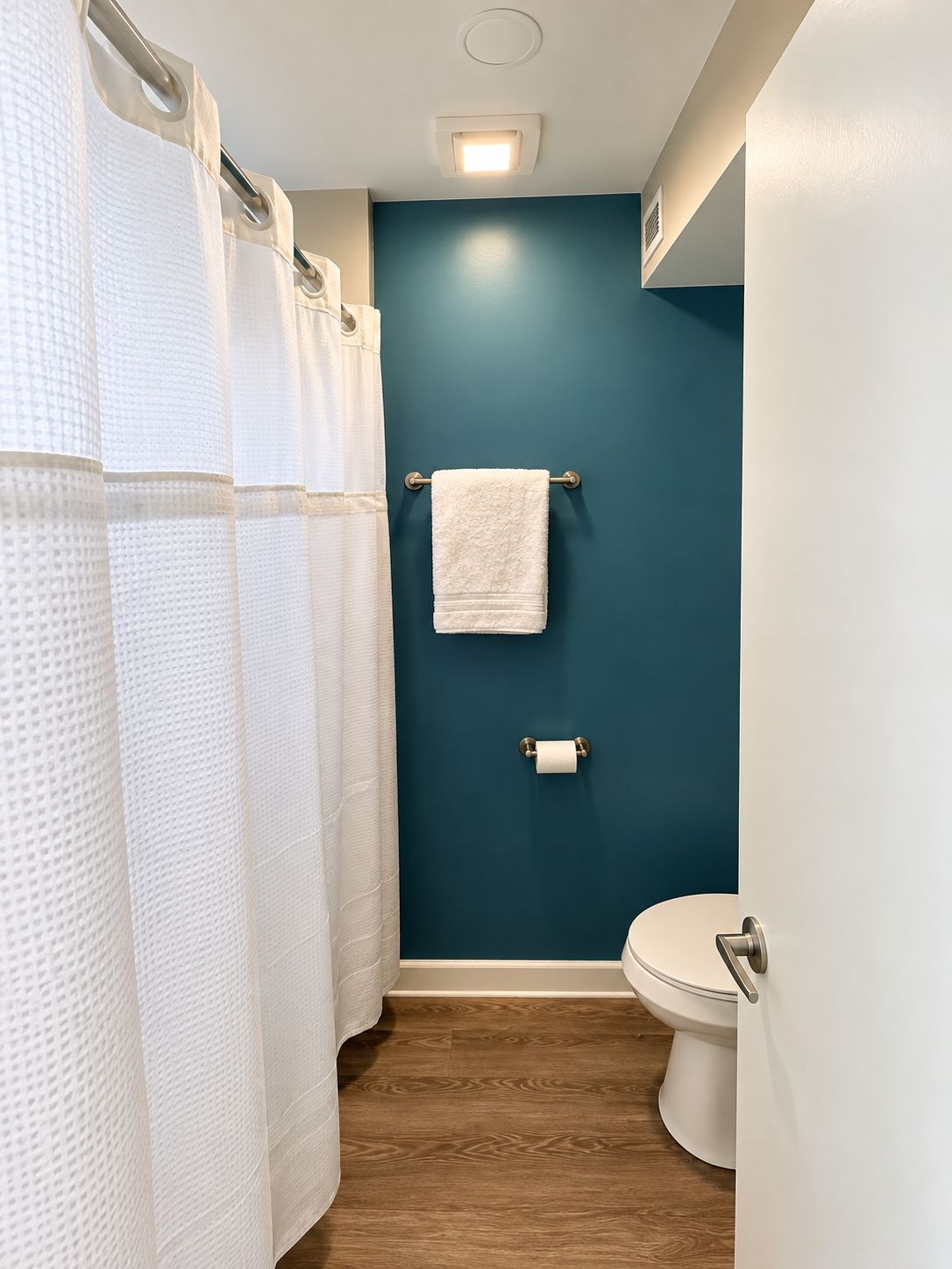 A bathroom with a blue wall, white toilet, and white shower curtains.