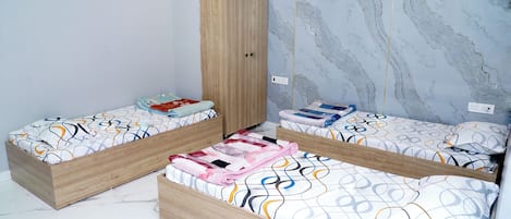 A bedroom with two wooden beds, marble-patterned walls, and a wardrobe.