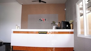 A reception desk with a logo, a TV, and a vase with flowers. - SRT Convention & Hotel (Tadpatri Rural)