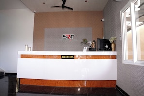 A reception desk with a logo, a TV, and a vase with flowers. - SRT Convention & Hotel (Tadpatri Rural)