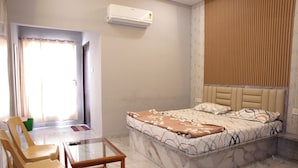 A hotel room with a bed, a glass table, two chairs, a small table, an air conditioning unit, and a curtain. - SRT Convention & Hotel (Tadpatri Rural)