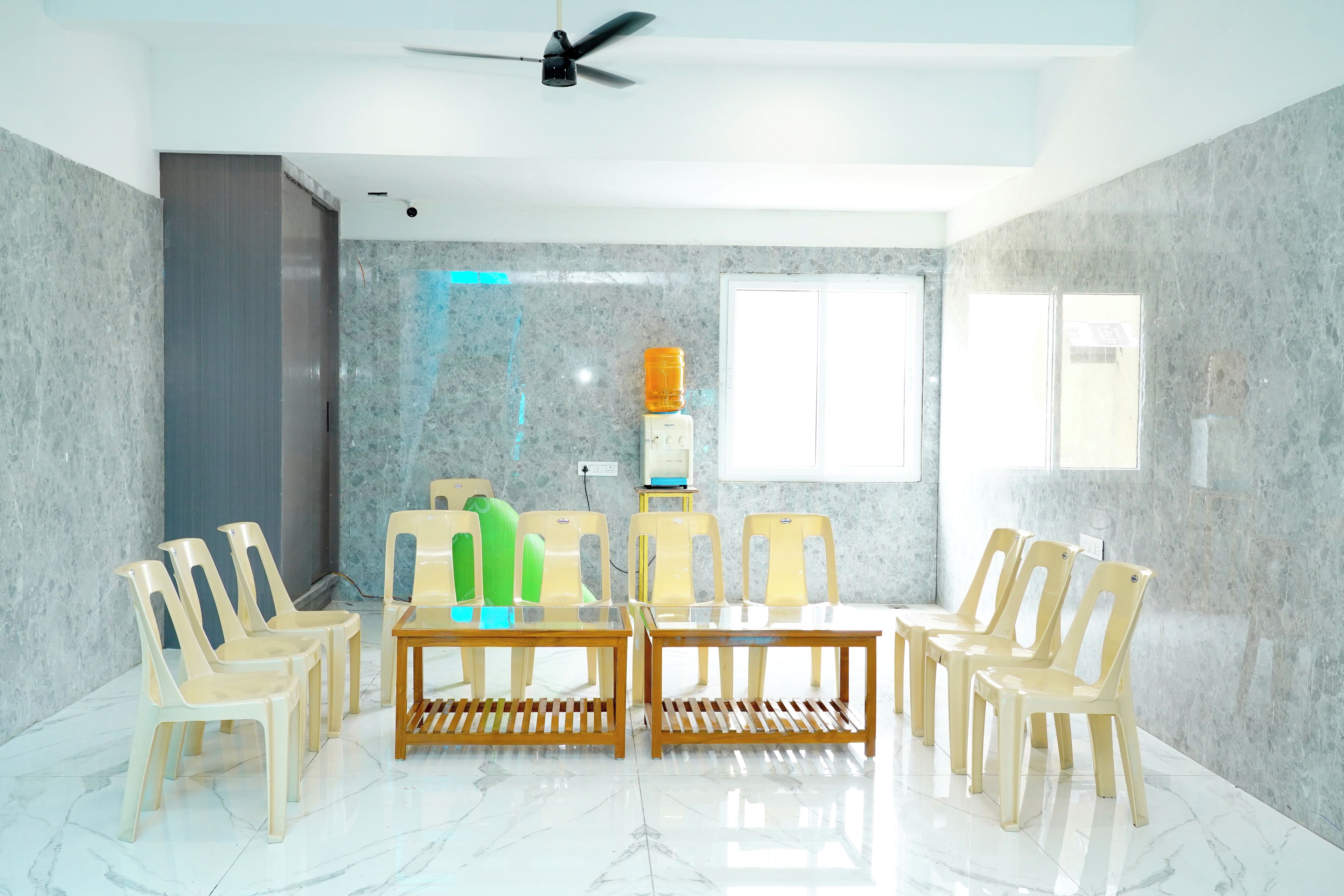 A room with a ceiling fan, a table with chairs, a water dispenser, and a window.