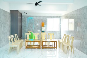 A room with a ceiling fan, a table with chairs, a water dispenser, and a window.