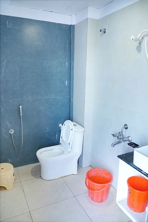 A bathroom with a toilet, a shower, and a sink. There are two buckets on the floor. - SRT Convention & Hotel (Tadpatri Rural)