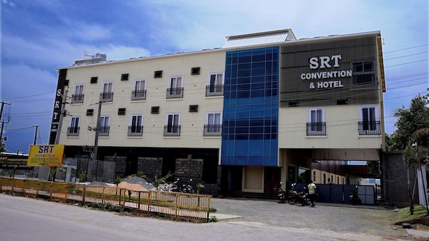 A building with multiple floors, a sign for 'SRT Convention & Hotel' on the side, and a gated entrance with parked motorcycles. - SRT Convention & Hotel (Tadpatri Rural)