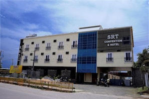 A building with multiple floors, a sign for 'SRT Convention & Hotel' on the side, and a gated entrance with parked motorcycles.