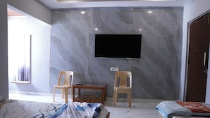 A bedroom with a bed, a TV mounted on the wall, and two chairs. - SRT Convention & Hotel (Tadpatri Rural)