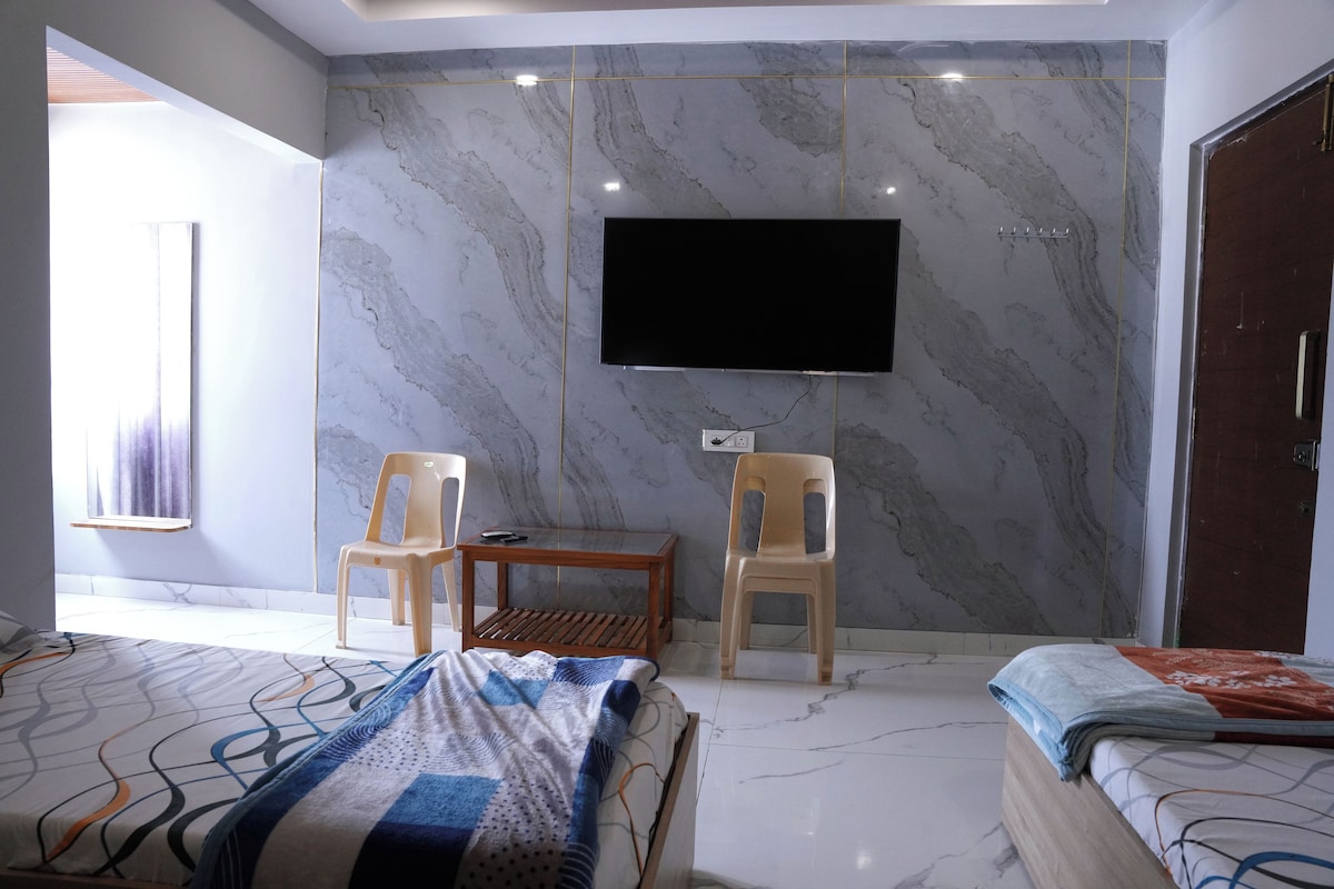 A bedroom with a bed, a TV mounted on the wall, and two chairs.