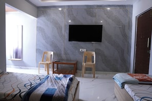 A bedroom with a bed, a TV mounted on the wall, and two chairs. - SRT Convention & Hotel (Tadpatri Rural)