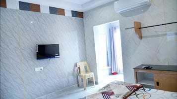 Habitació d'hotel amb televisió plana penjada a la paret, una cadira de fusta, un llit amb roba de llit estampada i un aparell d'aire condicionat.
