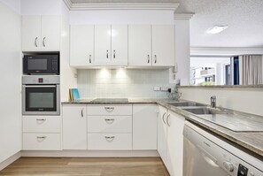 A modern kitchen with white cabinetry, a Bosch dishwasher, and a microwave. - 10/21 The Esplanade - A Coastal Escape in the Heart of Cotton Tree (Maroochydore)