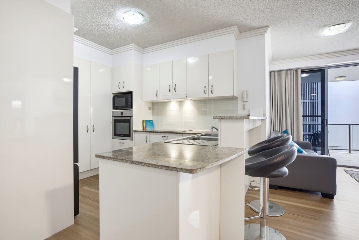 A modern kitchen with white cabinets, a granite countertop, and a built-in oven.