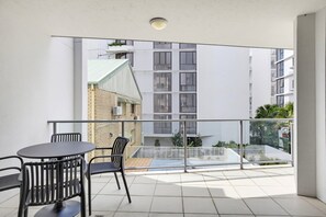 A balcony with a table and chairs, a view of a building with a striped facade, and a clear sky. - 10/21 The Esplanade - A Coastal Escape in the Heart of Cotton Tree (Maroochydore)