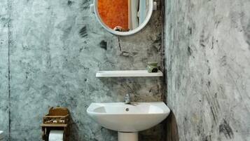 A bathroom with a white sink, a mirror, and a trash bin.