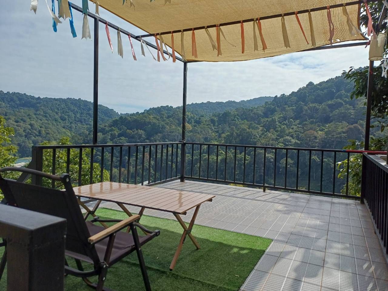 A terrace with a table and chairs, a view of a forested landscape, and a safety railing.