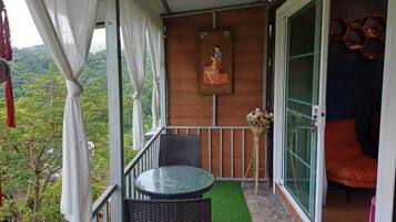 A balcony with a table and chairs, a painting on the wall, and a view of greenery.