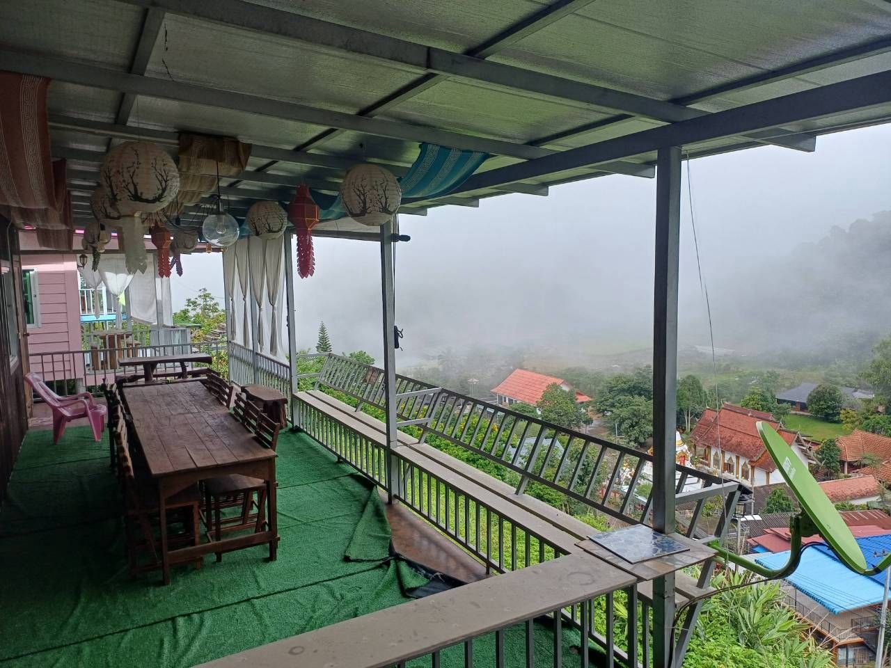 A covered outdoor seating area with a table and chairs, a railing, and a view of a foggy landscape.