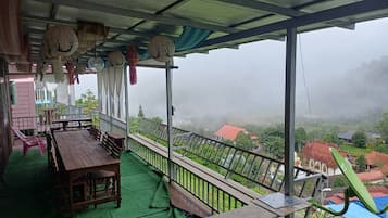 A covered outdoor seating area with a table and chairs, a railing, and a view of a foggy landscape.
