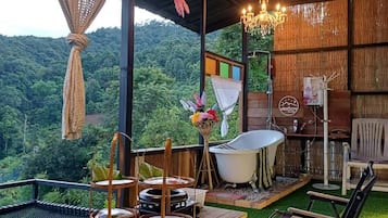 A wooden deck with a bathtub, a table, and chairs, overlooking a lush green landscape.