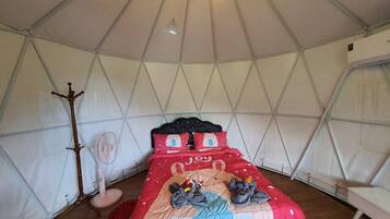 A tent with a bed, a fan, and a lamp.
