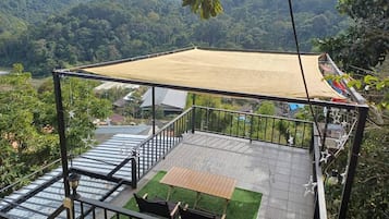 A balcony with a view of a mountainous landscape, a table and chairs, and a hanging chair.