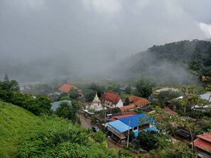 Un pueblo con un edificio blanco destacado y una cúpula dorada, rodeado de casas con tejados rojos, frente a un telón de fondo de vegetación exuberante y una montaña brumosa.