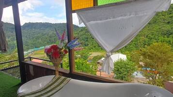 A bathtub in a room with a view of a lush landscape.