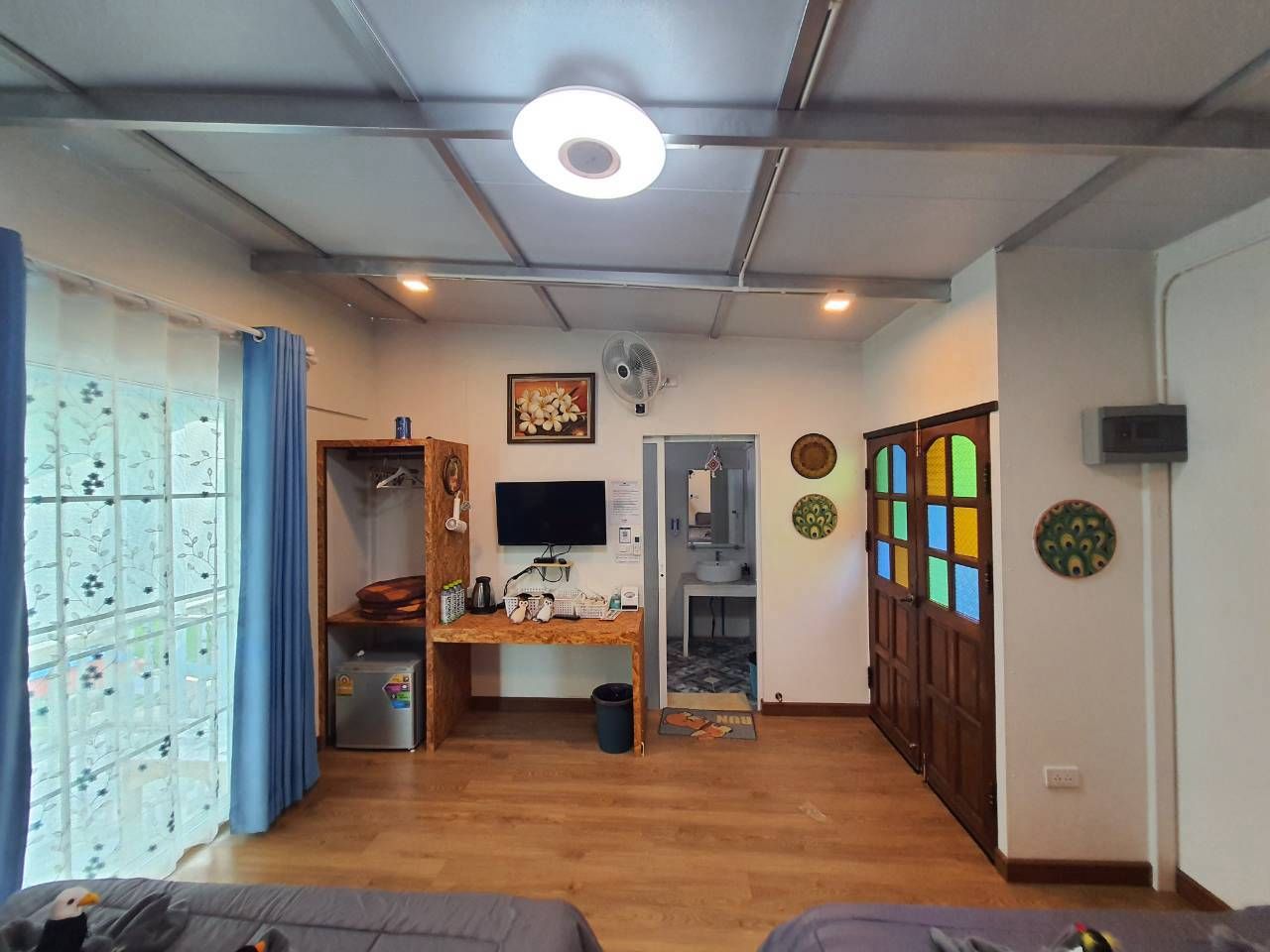 A compact living space with a wooden desk, a television, a refrigerator, and a door leading to a bathroom.