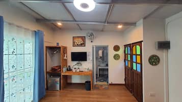 A compact living space with a wooden desk, a television, a refrigerator, and a door leading to a bathroom.