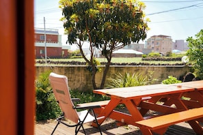 A wooden picnic table with a chair, a tree, and a view of buildings in the background.