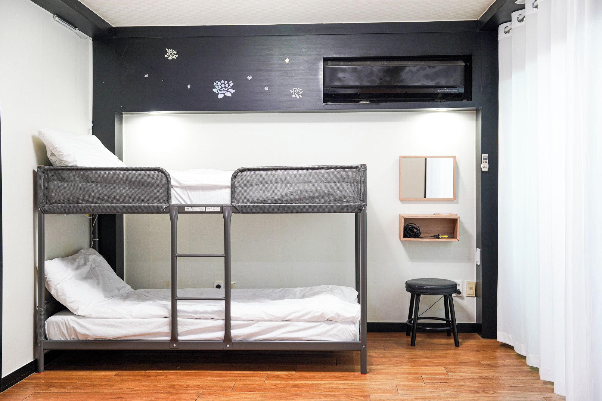 Quarto com beliche, TV fixada na parede, um banquinho e uma prateleira com objetos.
