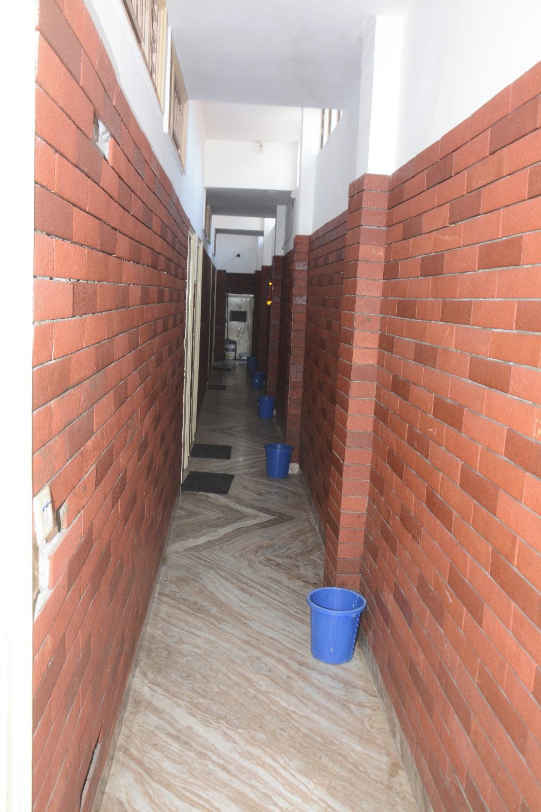 Un estrecho pasillo con paredes de ladrillo rojo y un piso con diseño, que conduce a una puerta al final.