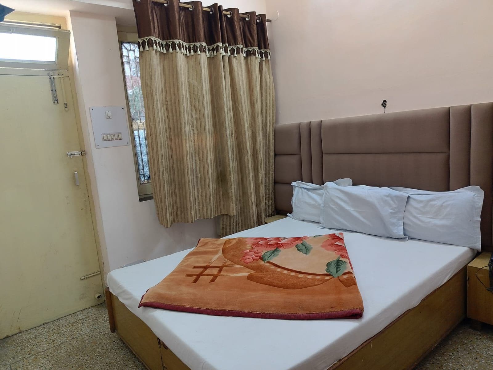 Un lit simple avec une tête de lit, une fenêtre avec des rideaux et une porte.