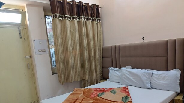 A single bed with a headboard, a window with curtains, and a door. - HOTEL SHIV VISHRAM (Haridwar)