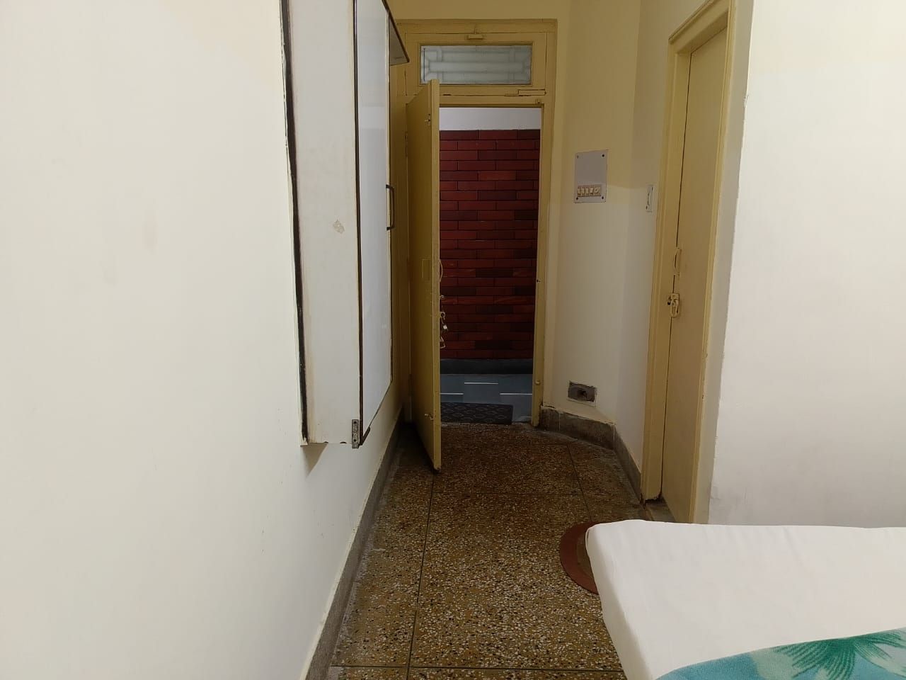 A narrow hallway with a door leading to a room with a red brick wall.